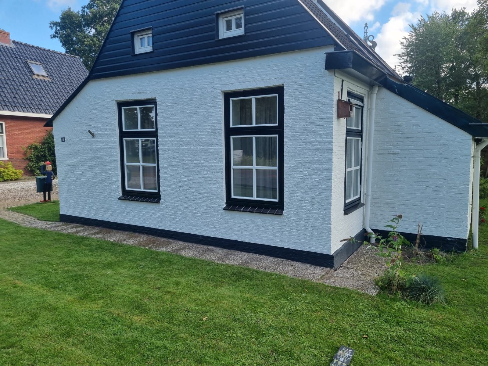 Een wit geschilderd huisje met zwarte kozijnen en een donker dak, na het schilderwerk