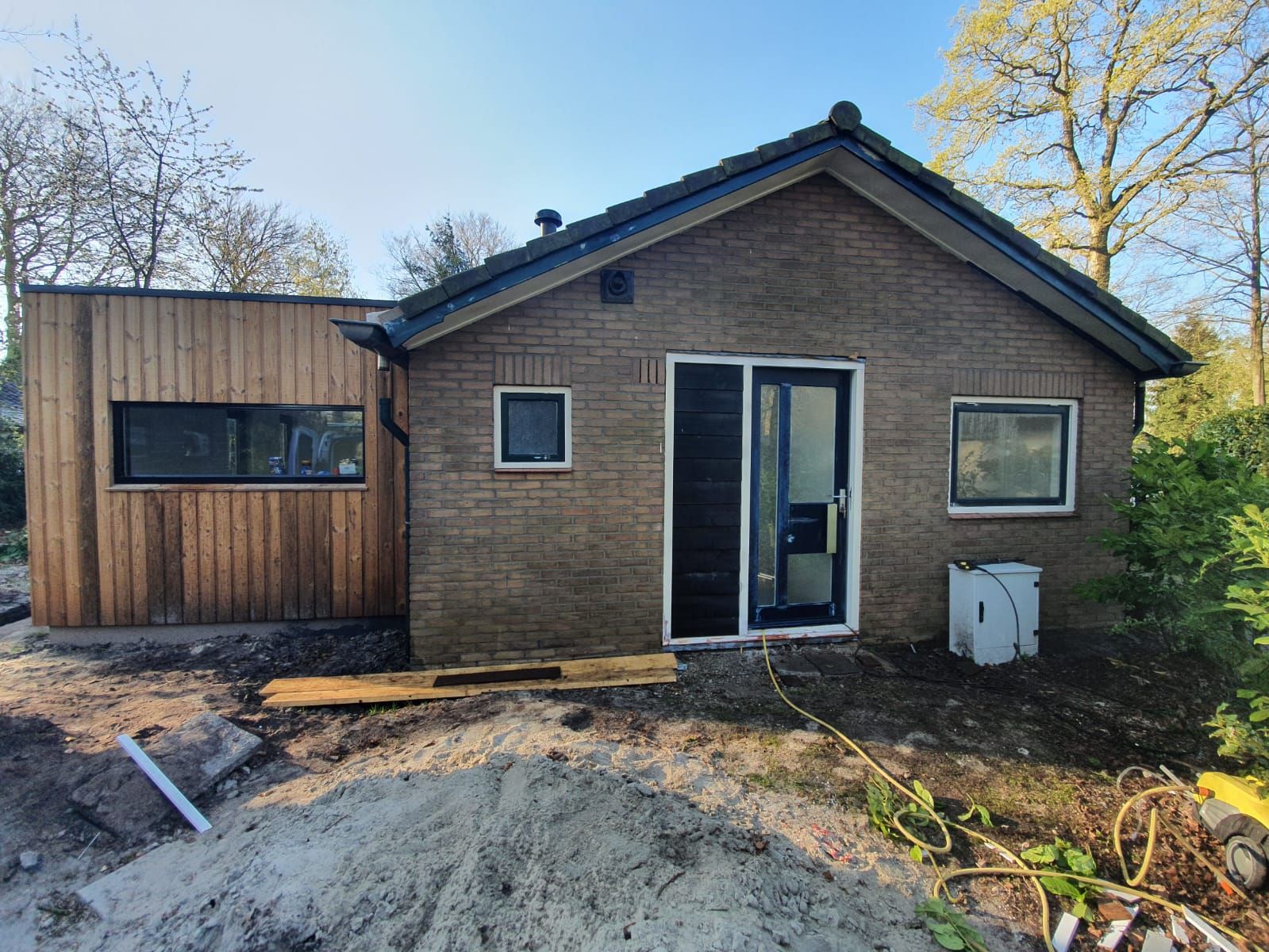 Een bakstenen bungalow met donkere kozijnen en een houten uitbouw