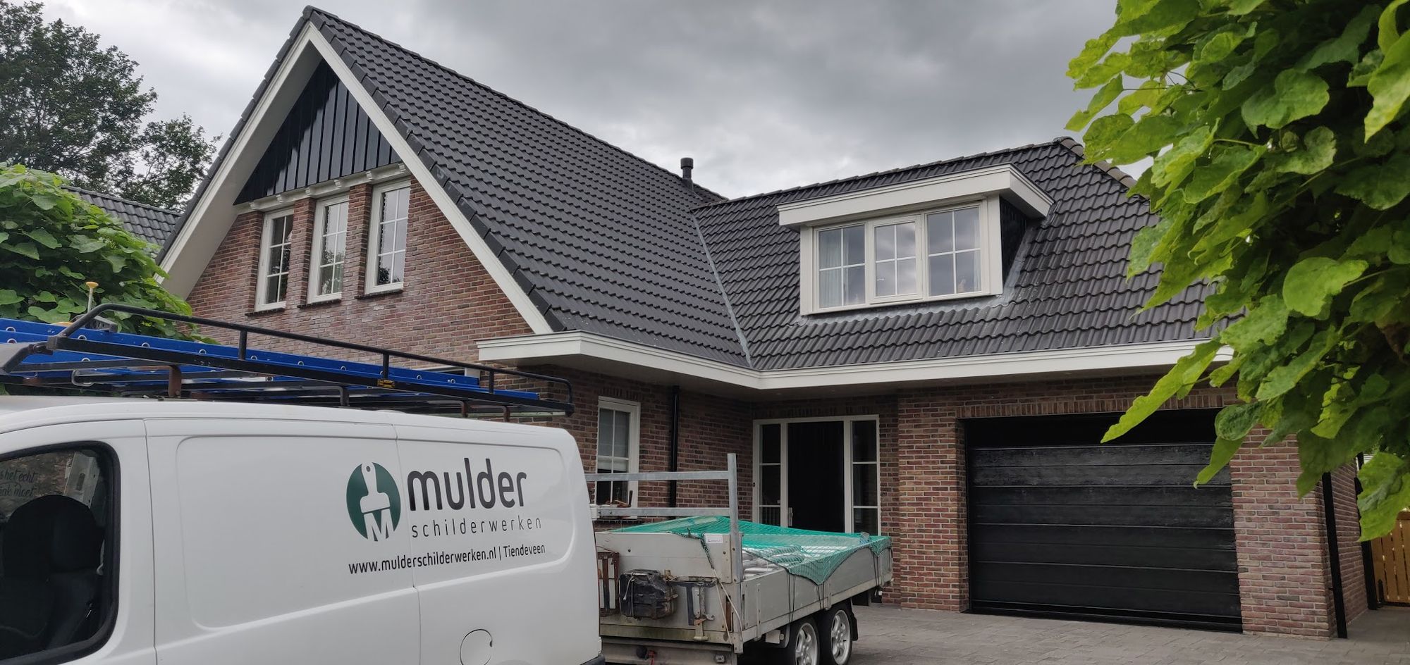De bus van Mulder schilderwerken met het logo, geparkeerd voor een huis met dakkapellen
