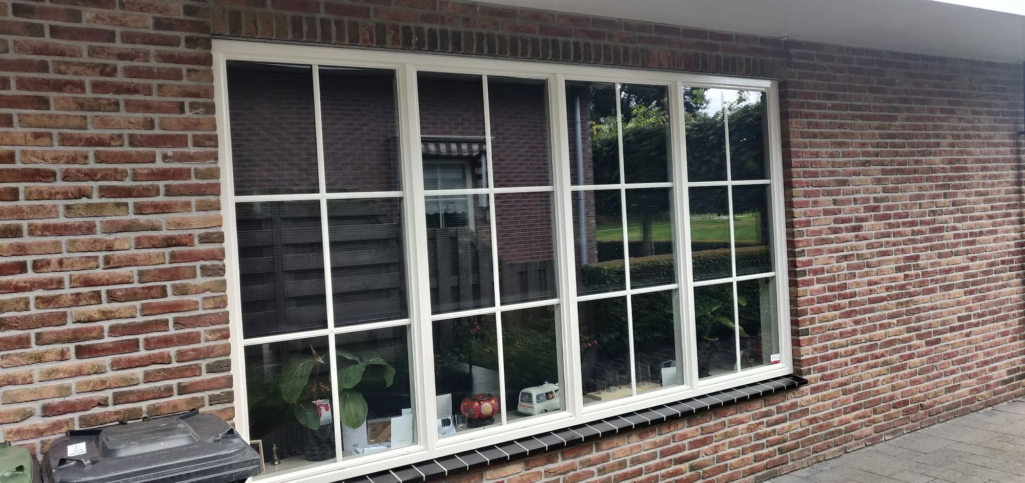 Een groot raam met wit geschilderde kozijnen en roeden in een rode bakstenen gevel
