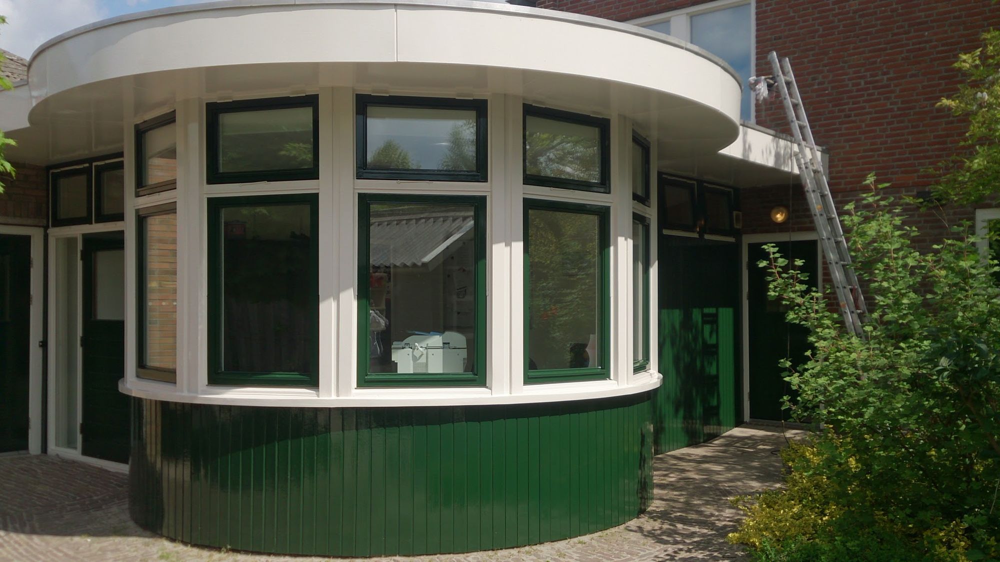 Een ronde erker met groene panelen en wit geschilderde boeidelen